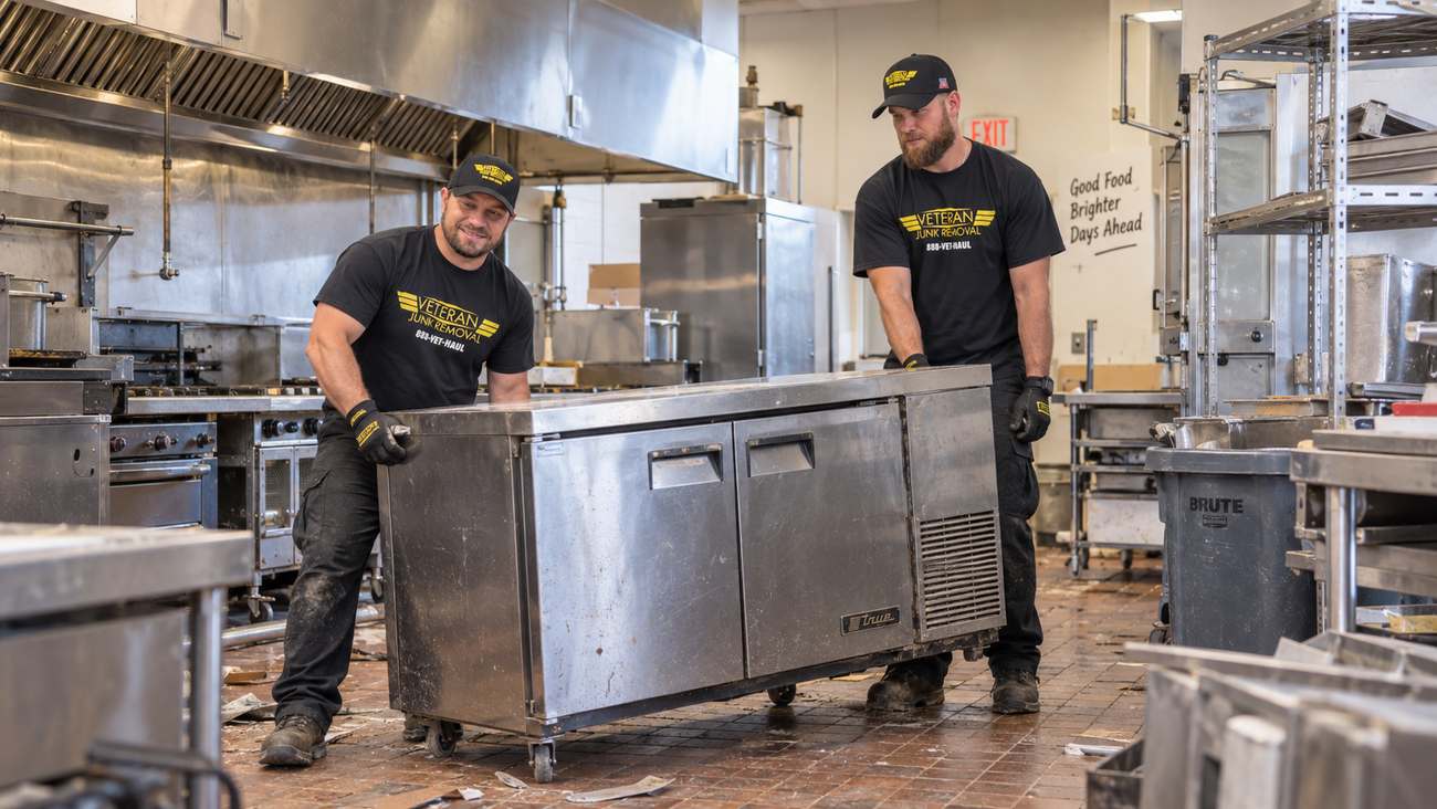 A Veteran Junk Removal crew member wheeling a stainless prep table out of a commercial kitchen